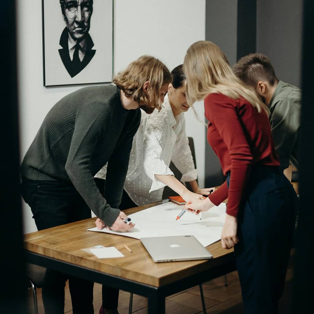 Four people around table with plans and a laptop